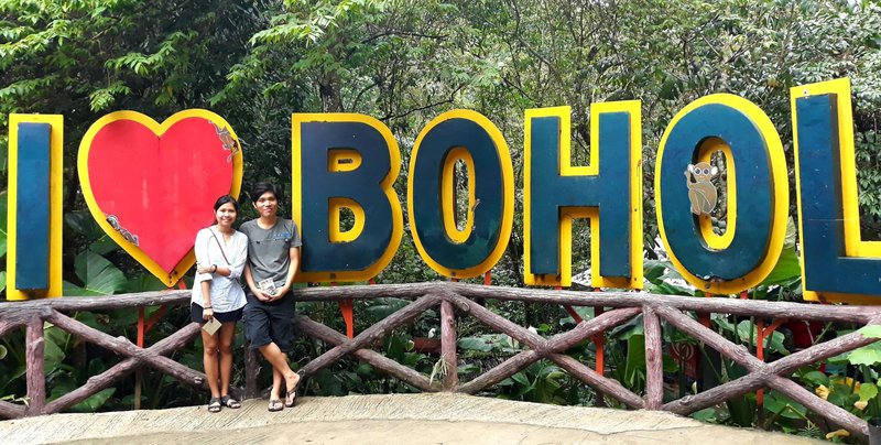 a young couple with a huge sign behind them saying 'I love Bohol'