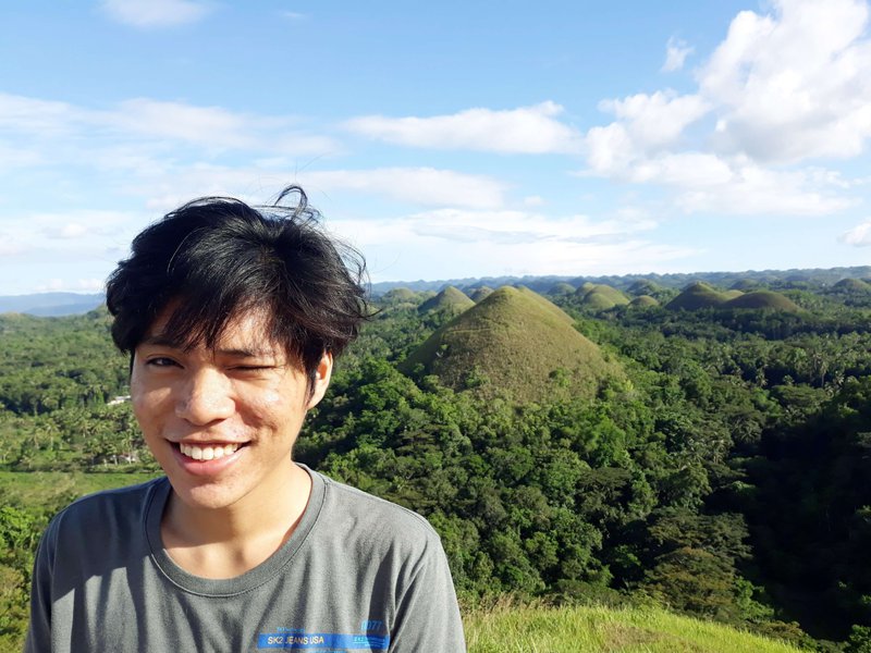a young man smiling, Chocolate Hills is his background
