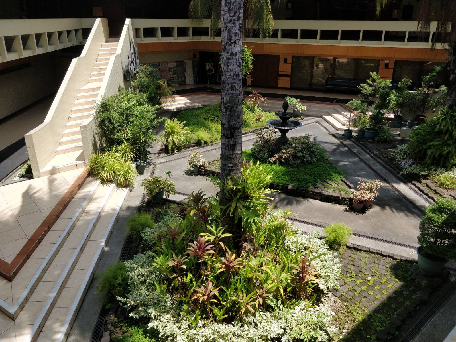Courtyard of a brutalist architecture; it's garden is blooming with flora.