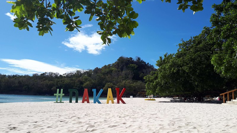 view of a white-sand beach with a huge sign saying Dakak